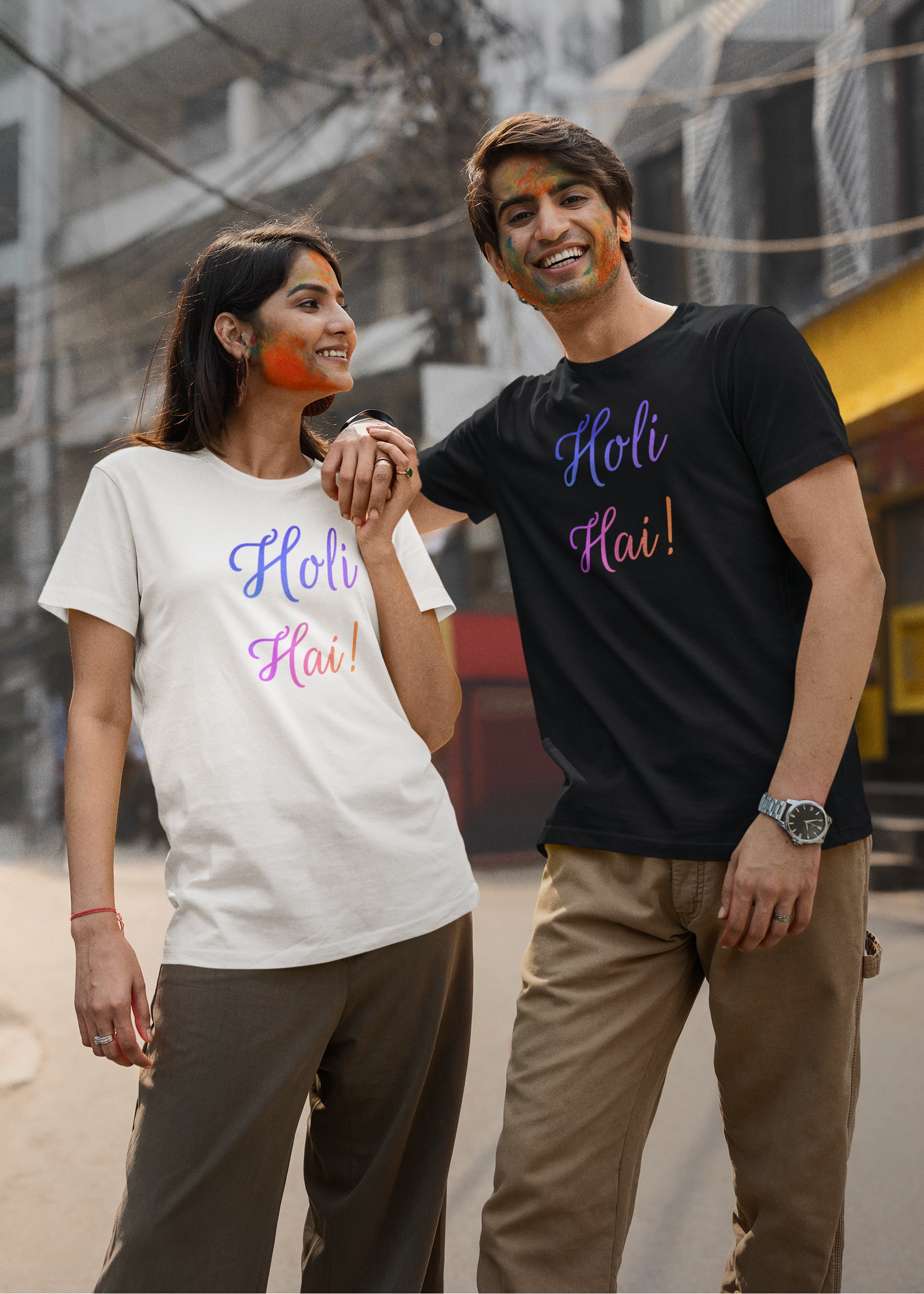 Two people wearing 'Holi Hai!' t-shirts standing together outdoors.